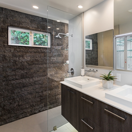 Dark brick effect wall in a shower with a dark wooden vanity unity for two white sinks.