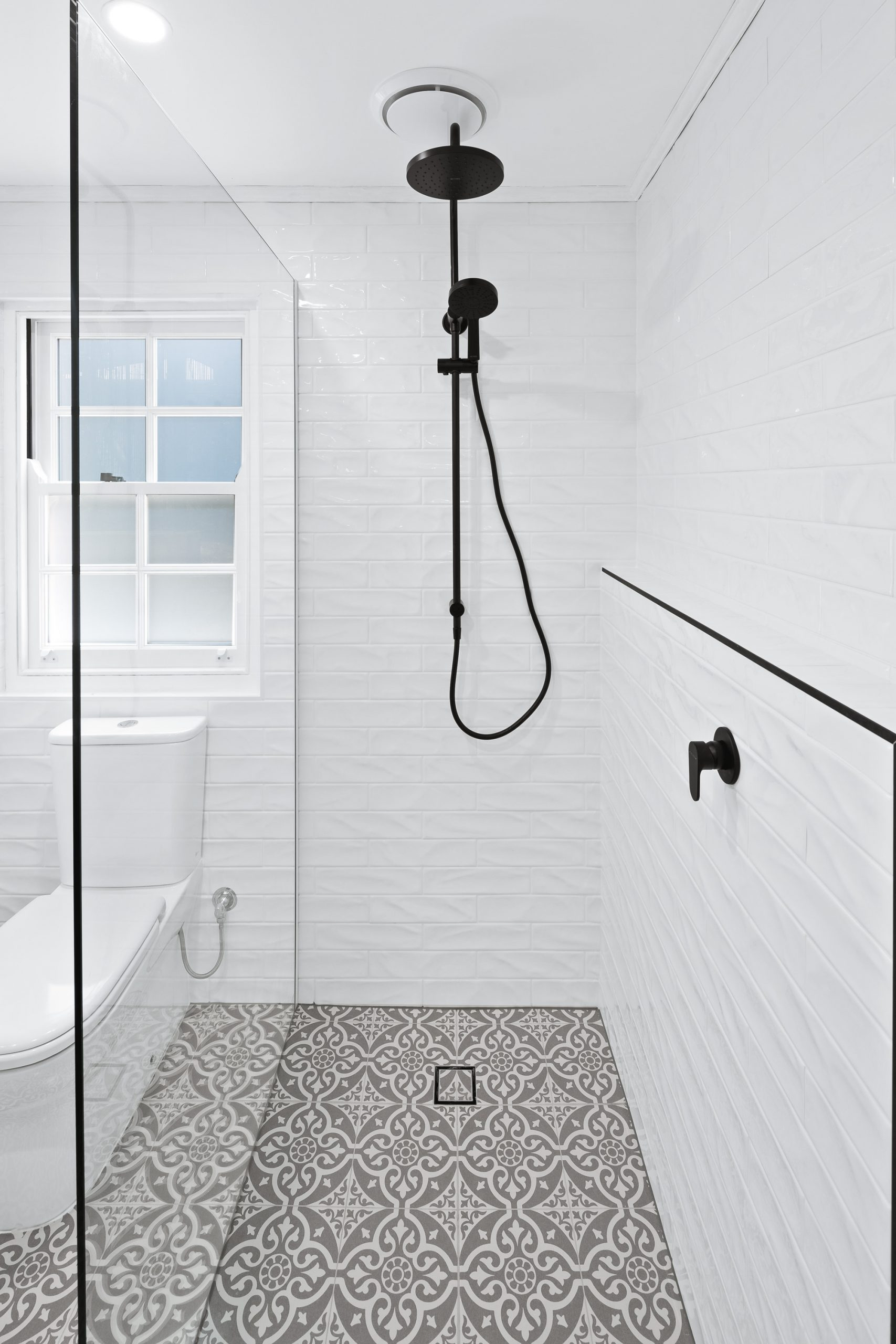 Patterned floor tiles and white subway tiles on the wall in a bright bathroom with black details
