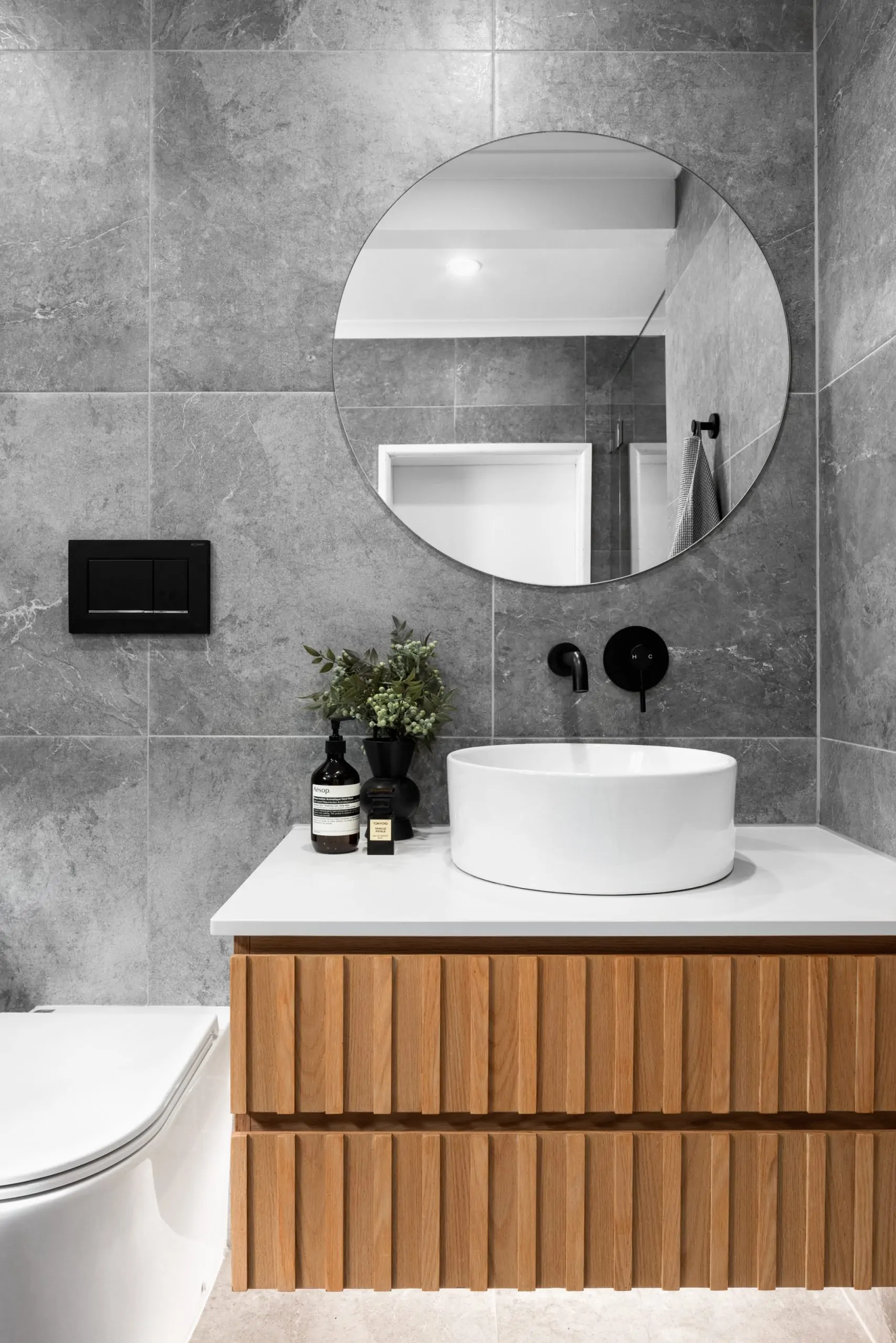 Large grey bathroom tiles, wooden vanity, large round mirror in a modern bathroom