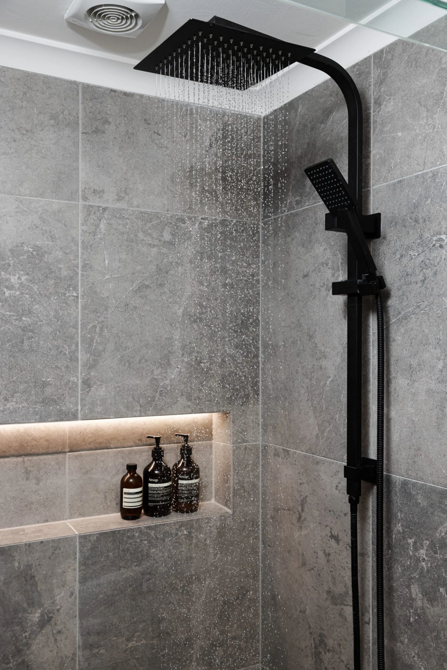Square rainfall shower in black with a bathroom niche with products