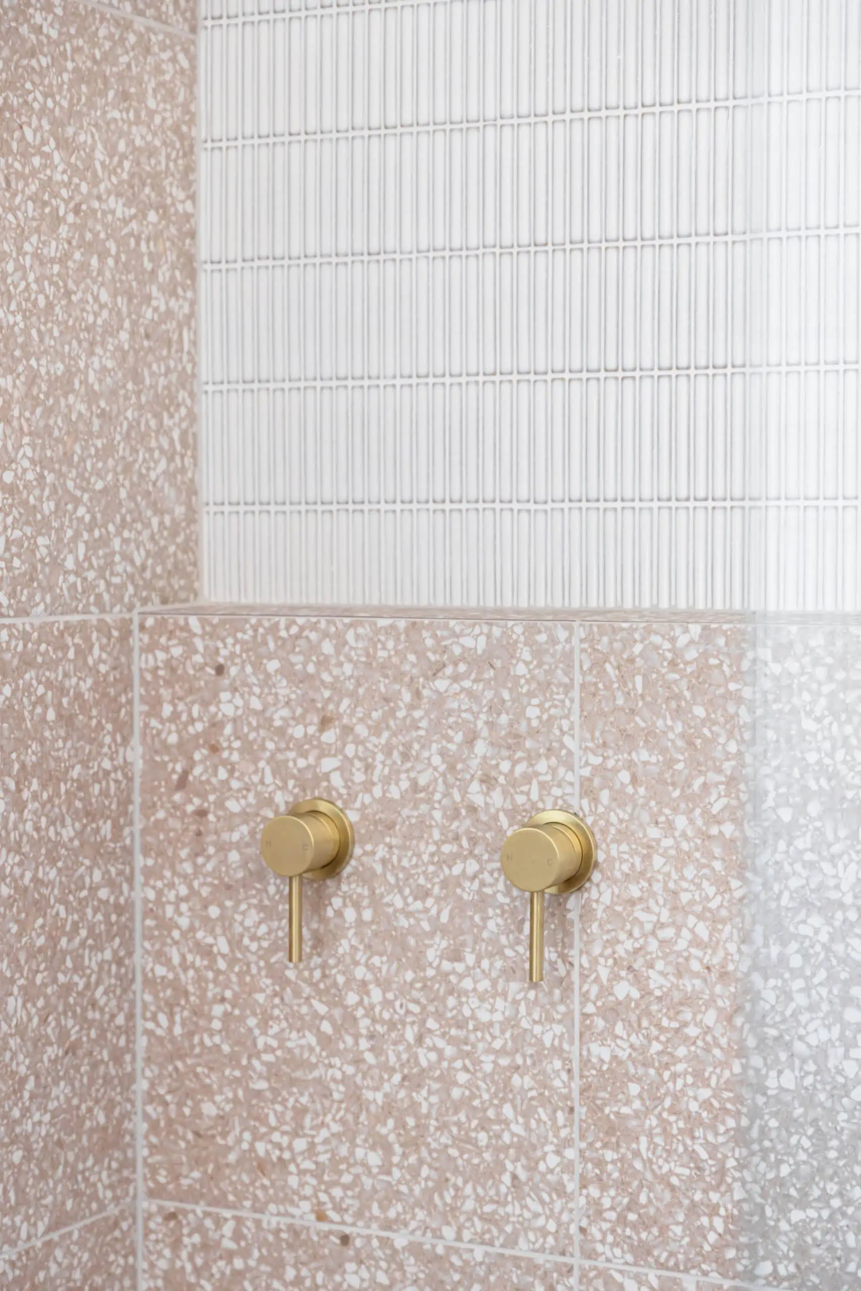 Gold taps on blush pink granite tiles with white finger tiles above in a new shower.