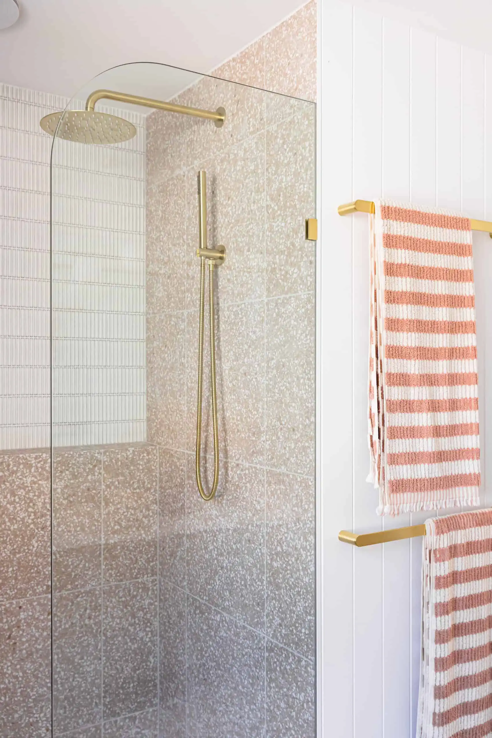 Bathroom renovation after photo showing the shower area with gold accessories and blush pink and white towels.