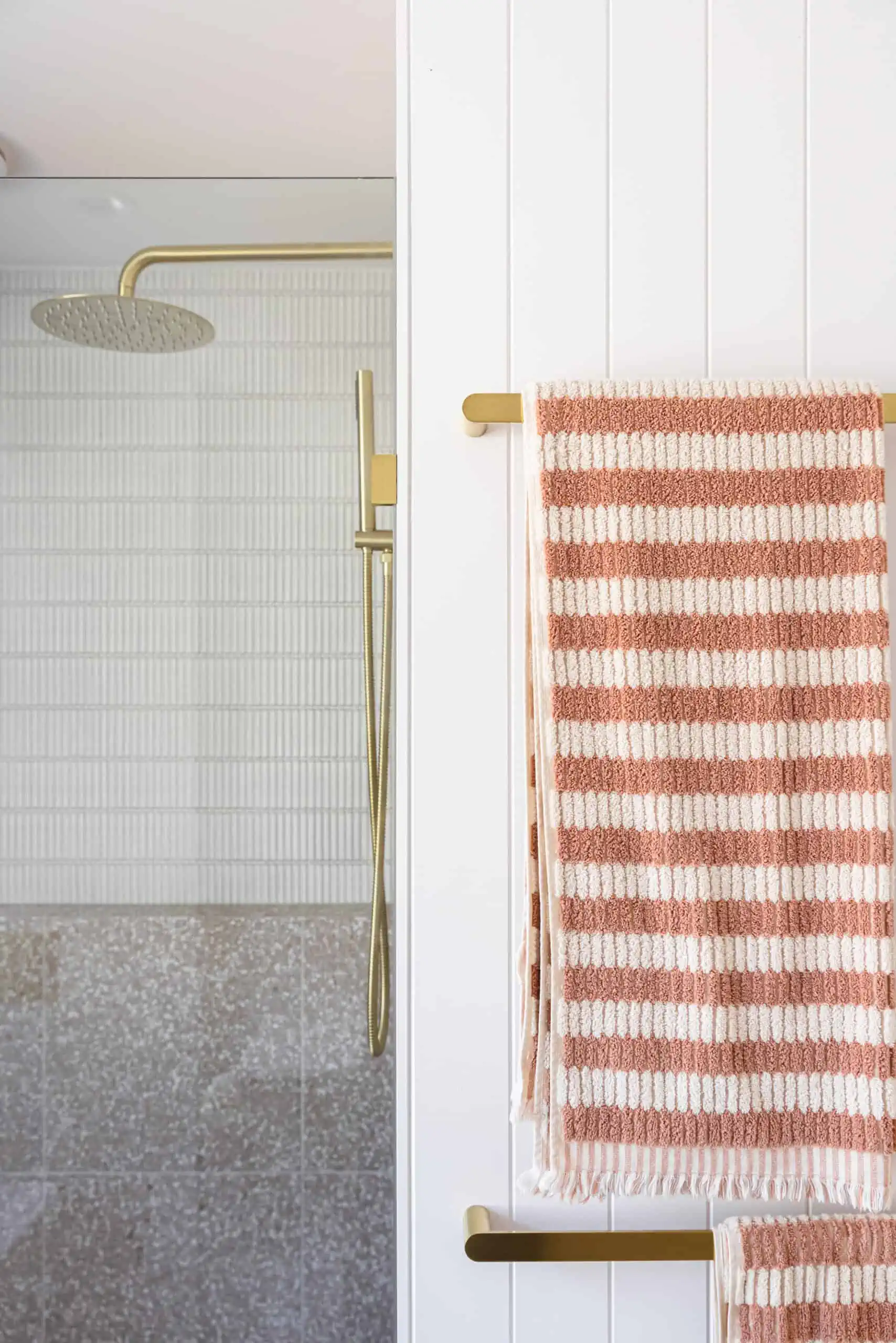 Bathroom renovation after shot showing a shower with gold accessories and a striped towel.