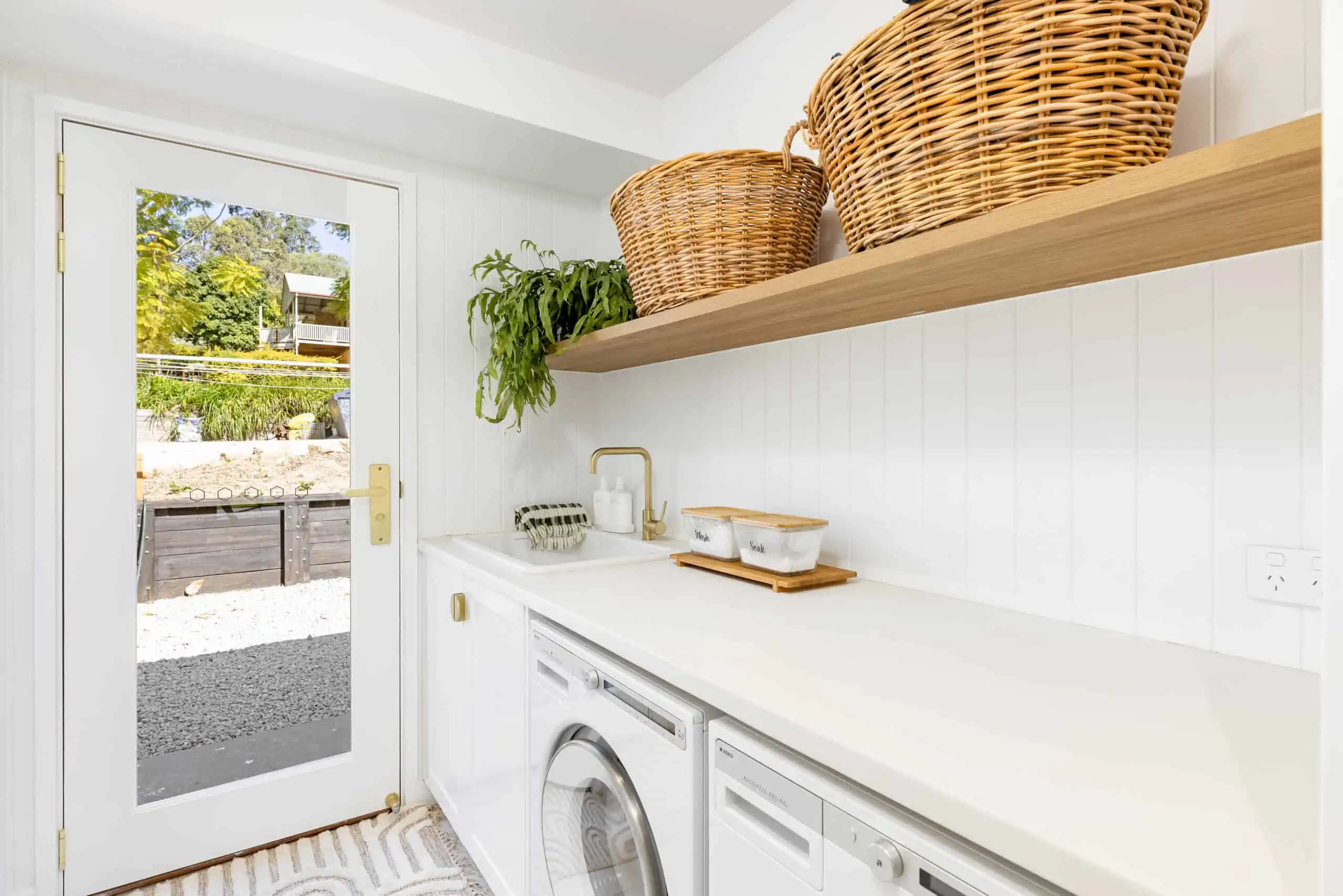 Modern white utility area with wooden shelves with baskets and a plant.
