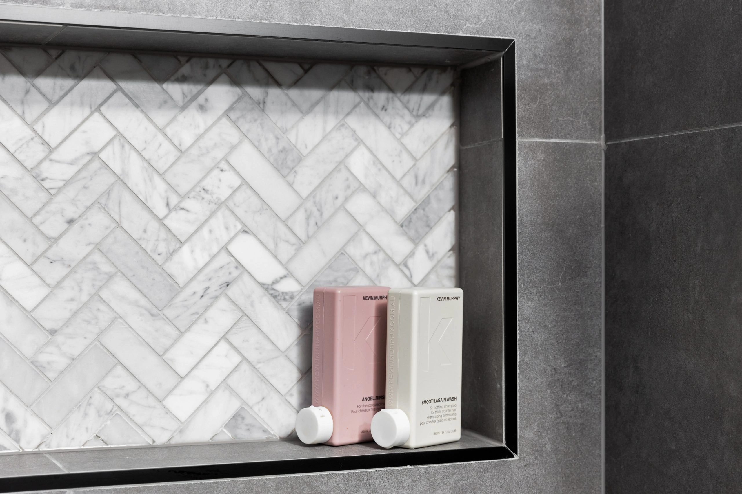 Dark grey bathroom tiles with a shower niche containing products