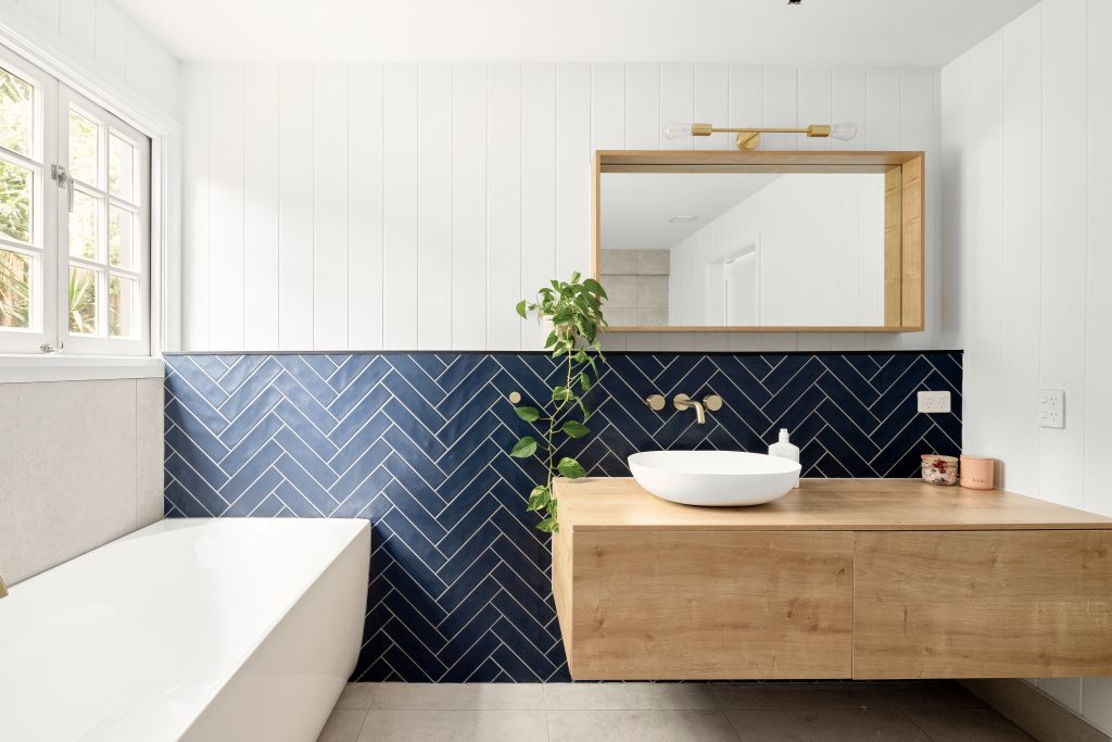 Blue herringbone bathroom tiles with a wooden vanity and white bath