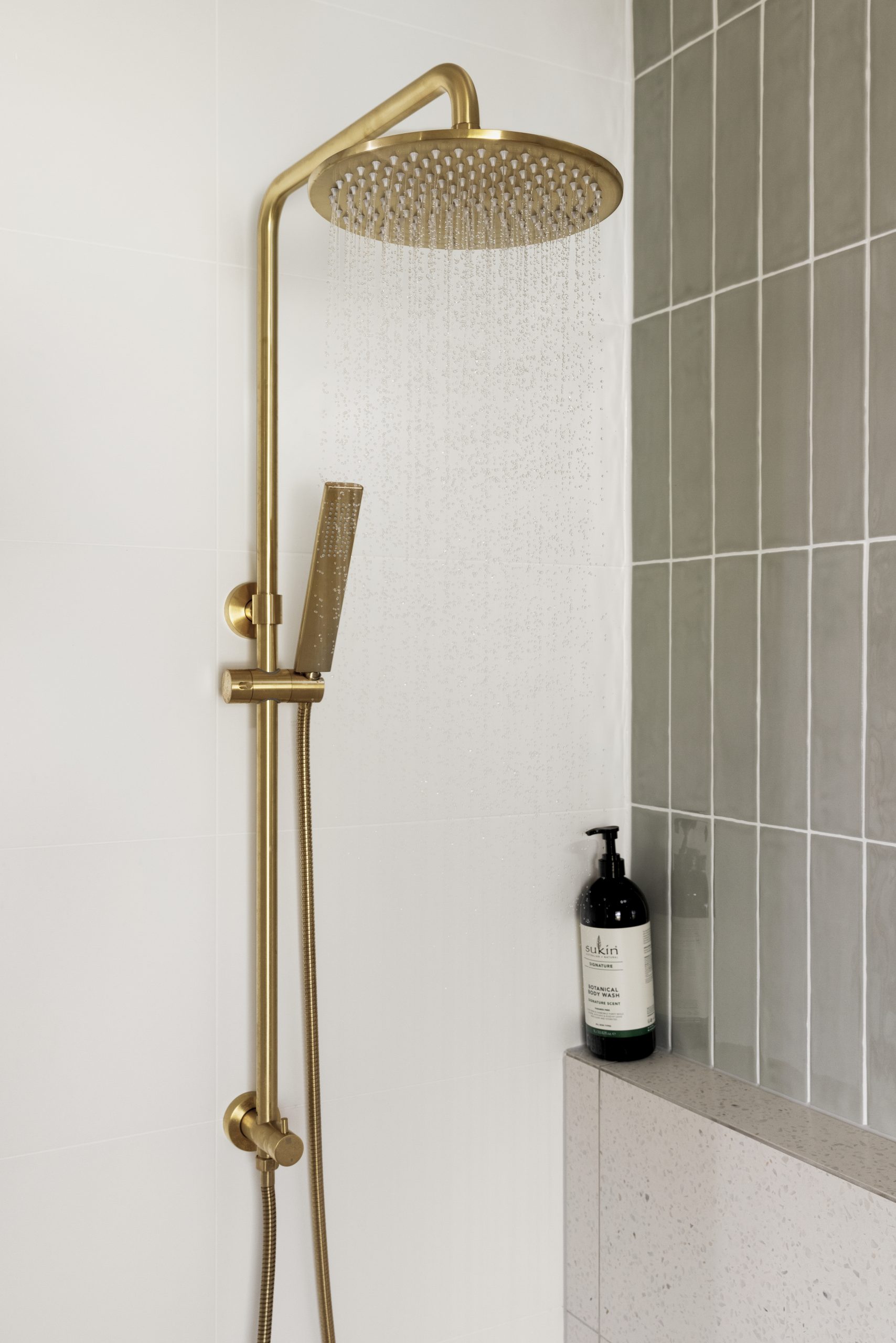 Gold coloured shower on white bathroom tiles alongside sage coloured tiles