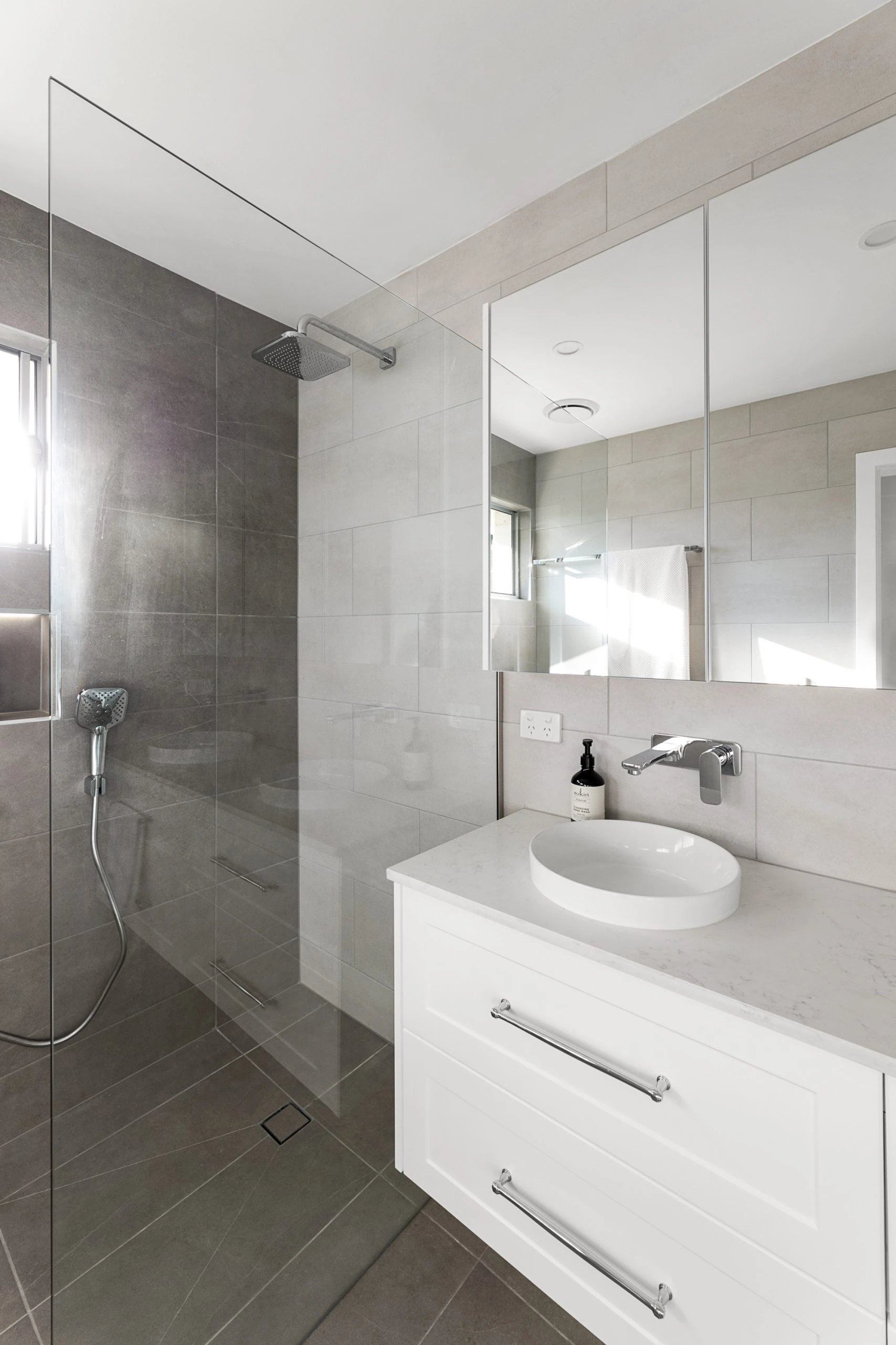 White vanity unit in a modern bathroom featuring a clean class shower screen