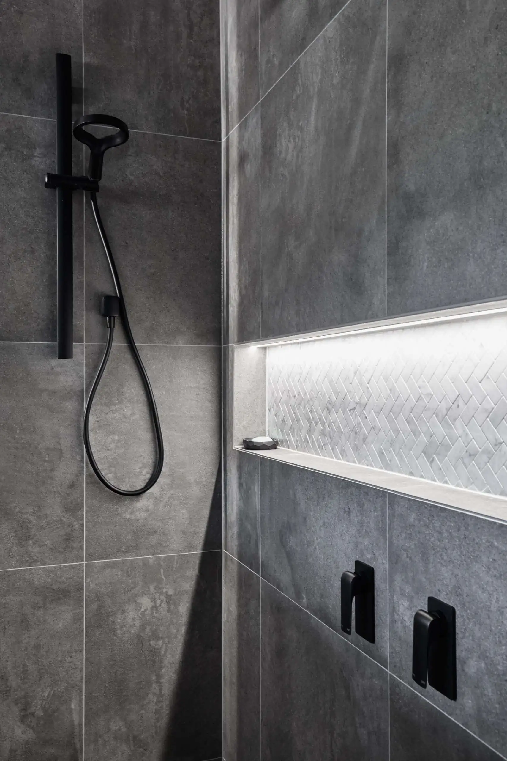 Large grey wall tiles in a modern bathroom featuring a shower niche and black details