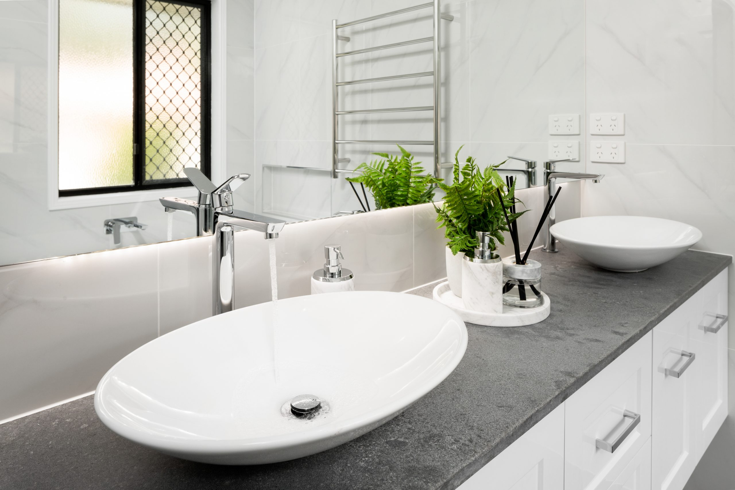 White bathroom with a dark grey unit top featuring two white sinks