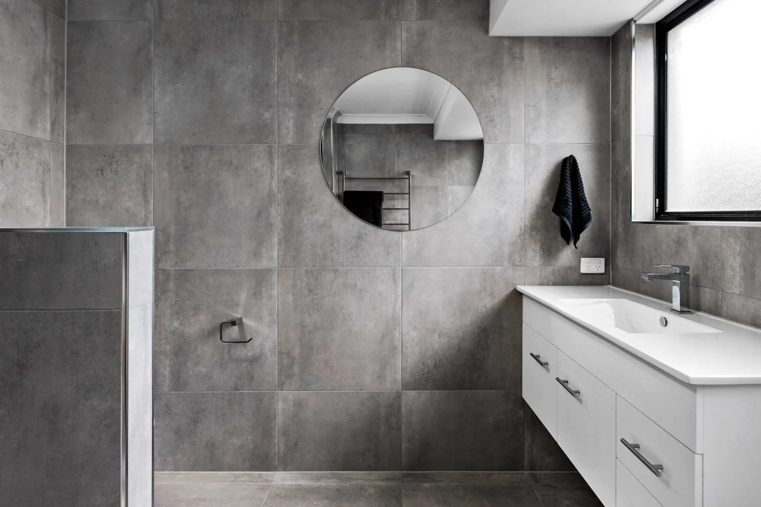 Modern bathroom design with a large round mirror and white vanity unit
