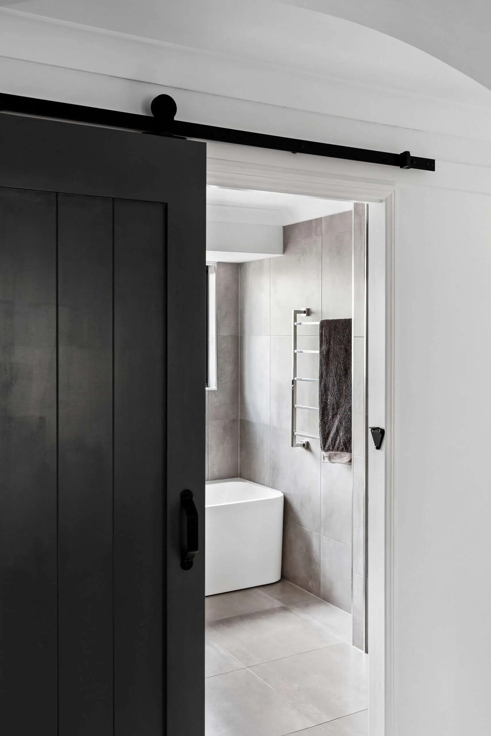Dark sliding door opening to reveal a modern bathroom with chrome details