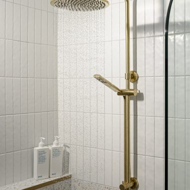 Gold wall mounted shower on white tiles