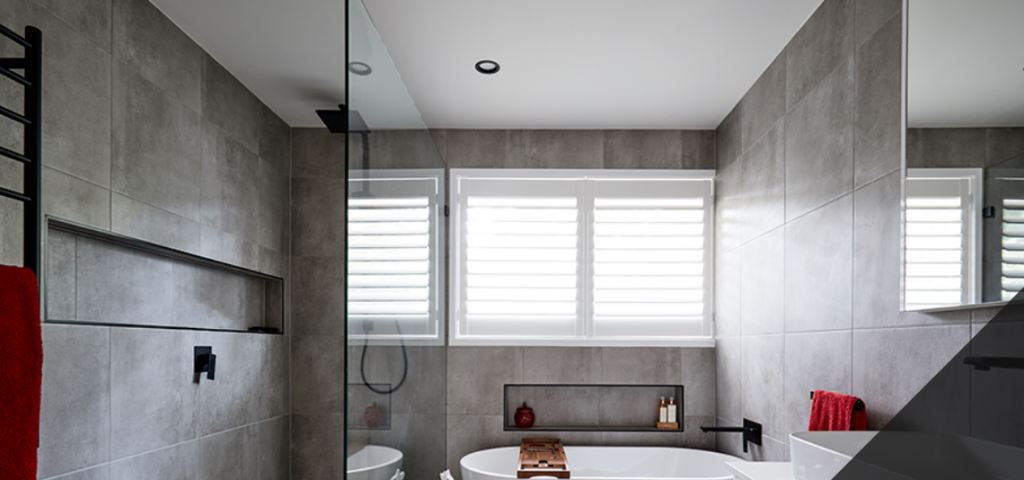 Photograph of a modern bathroom with a white bath and grey wall tiles