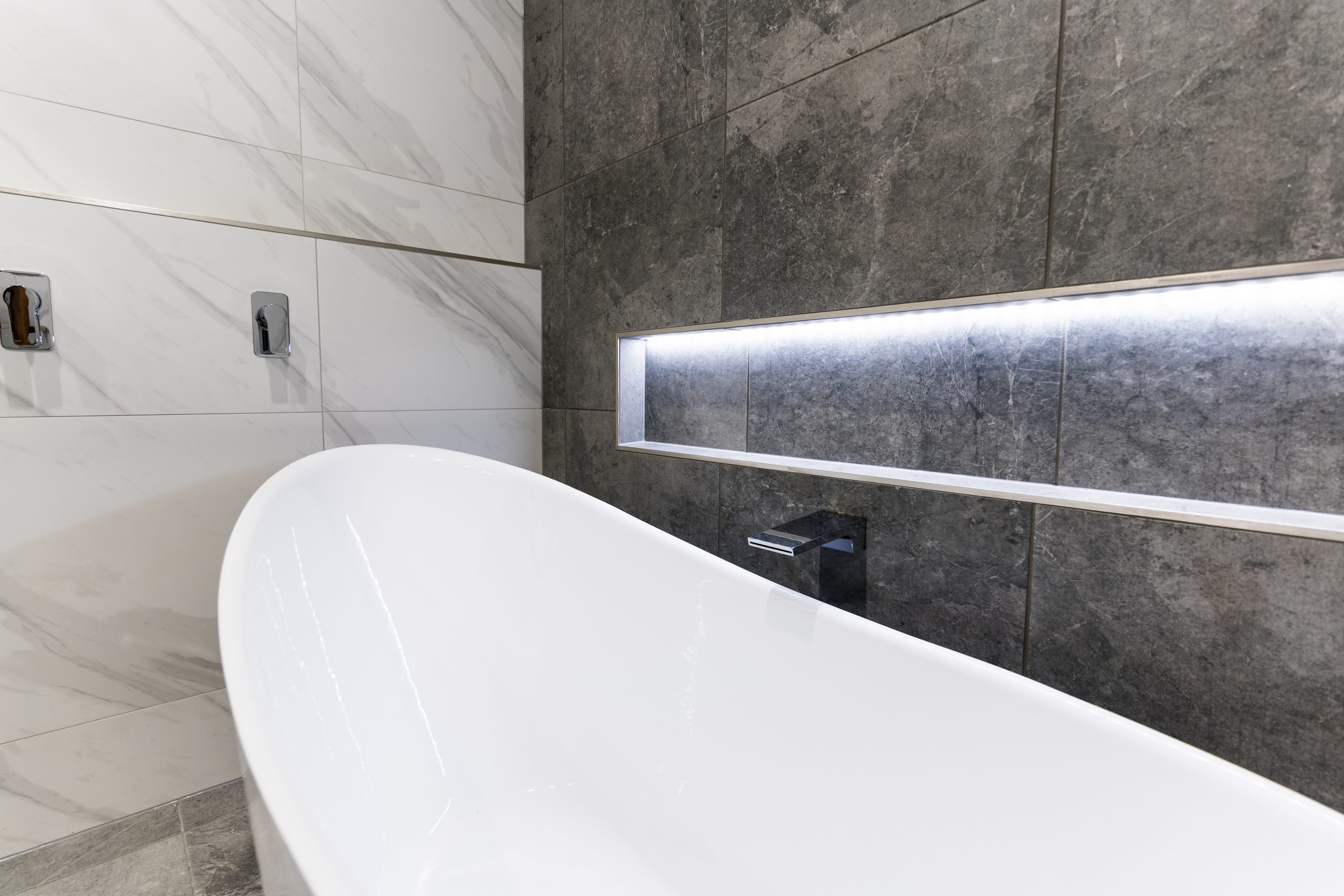 White bath next to a wall with a niche for bathroom products in a modern bathroom