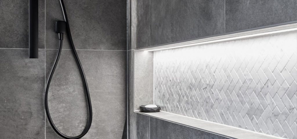 Shower niche with a herringbone tile background next to a black shower unit.